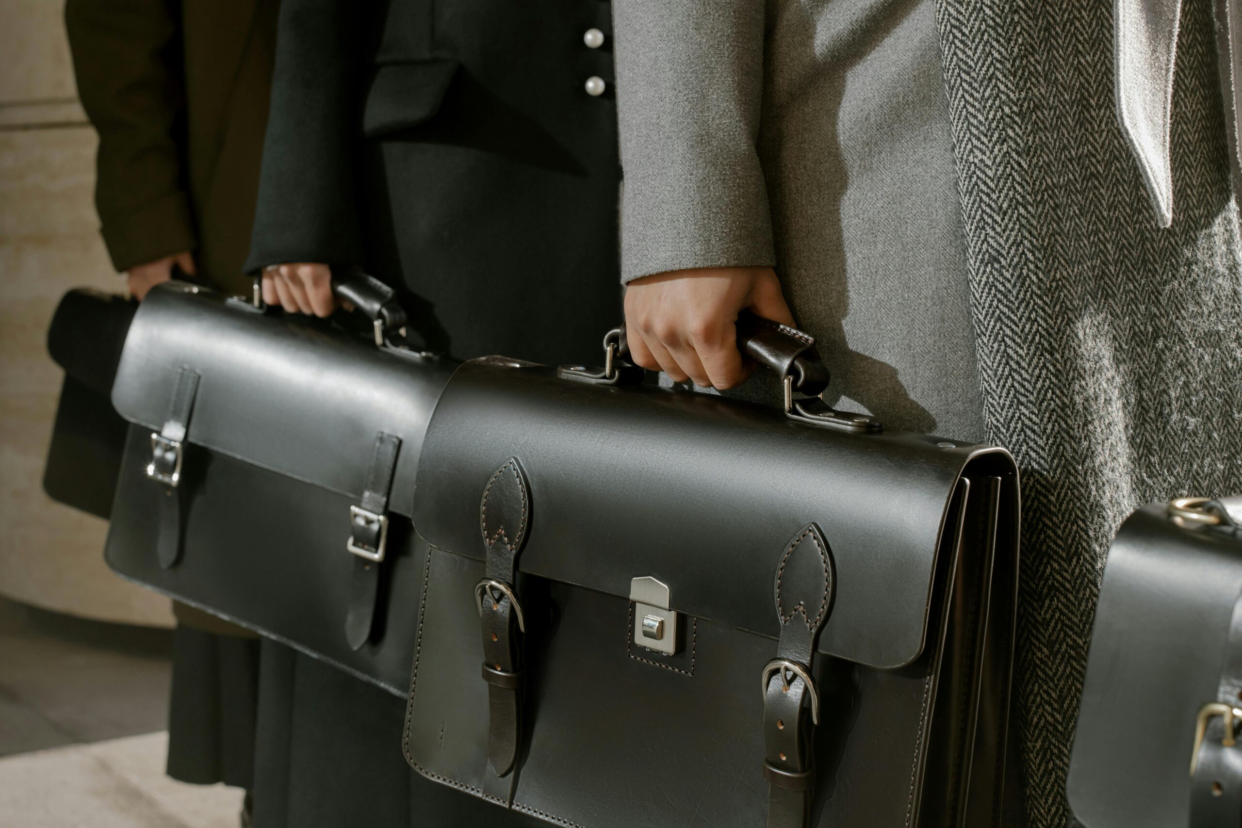 Row of professionals in formal coats holding structured black leather briefcases with silver buckles and clasps.